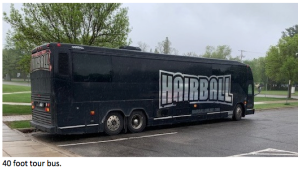 Large black tour bus with the word ‘HAIRBALL’ displayed in bold silver letters is parked along a rainy street lined with green trees. Text at the bottom reads: ‘40 foot tour bus.